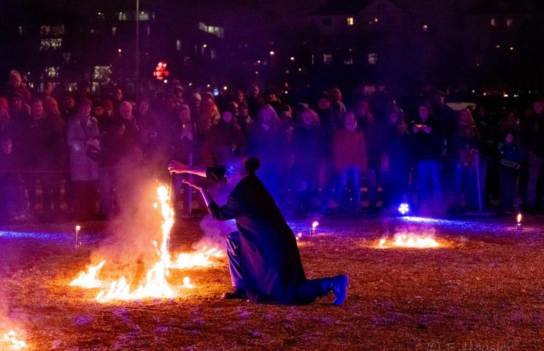 Künstler zündet Feuer vor großer Menschenmenge bei nächtlicher Veranstaltung.