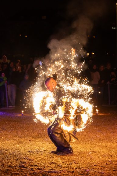 Feuerperformer mit großen Flammen vor einem Publikum im Hintergrund.