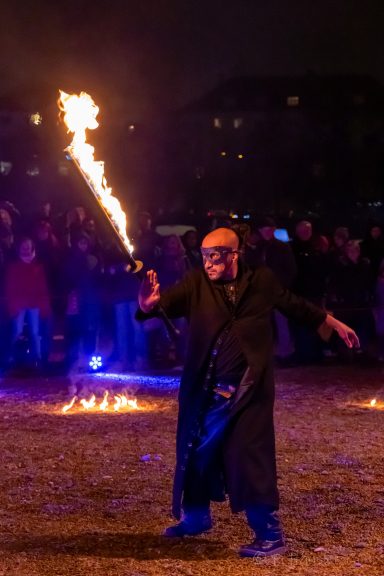 Ein Künstler mit Fackel performt vor einer Menschenmenge bei Nacht.